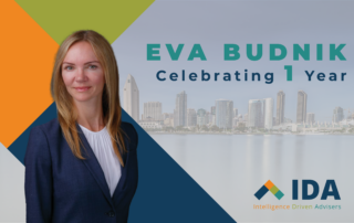 Eva Budnik celebrates one year at Intelligence Driven Advisers, with a professional portrait in front of a city skyline and the IDA logo
